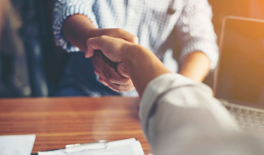 people shaking hands over a desk, paperwork visible beneath